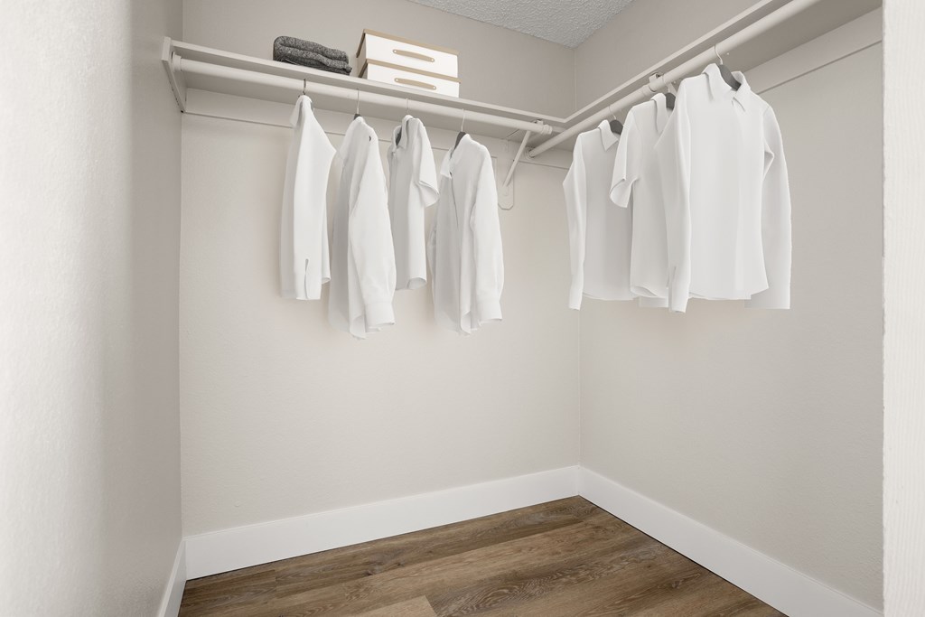 a walk in closet with white clothes hanging on a rail